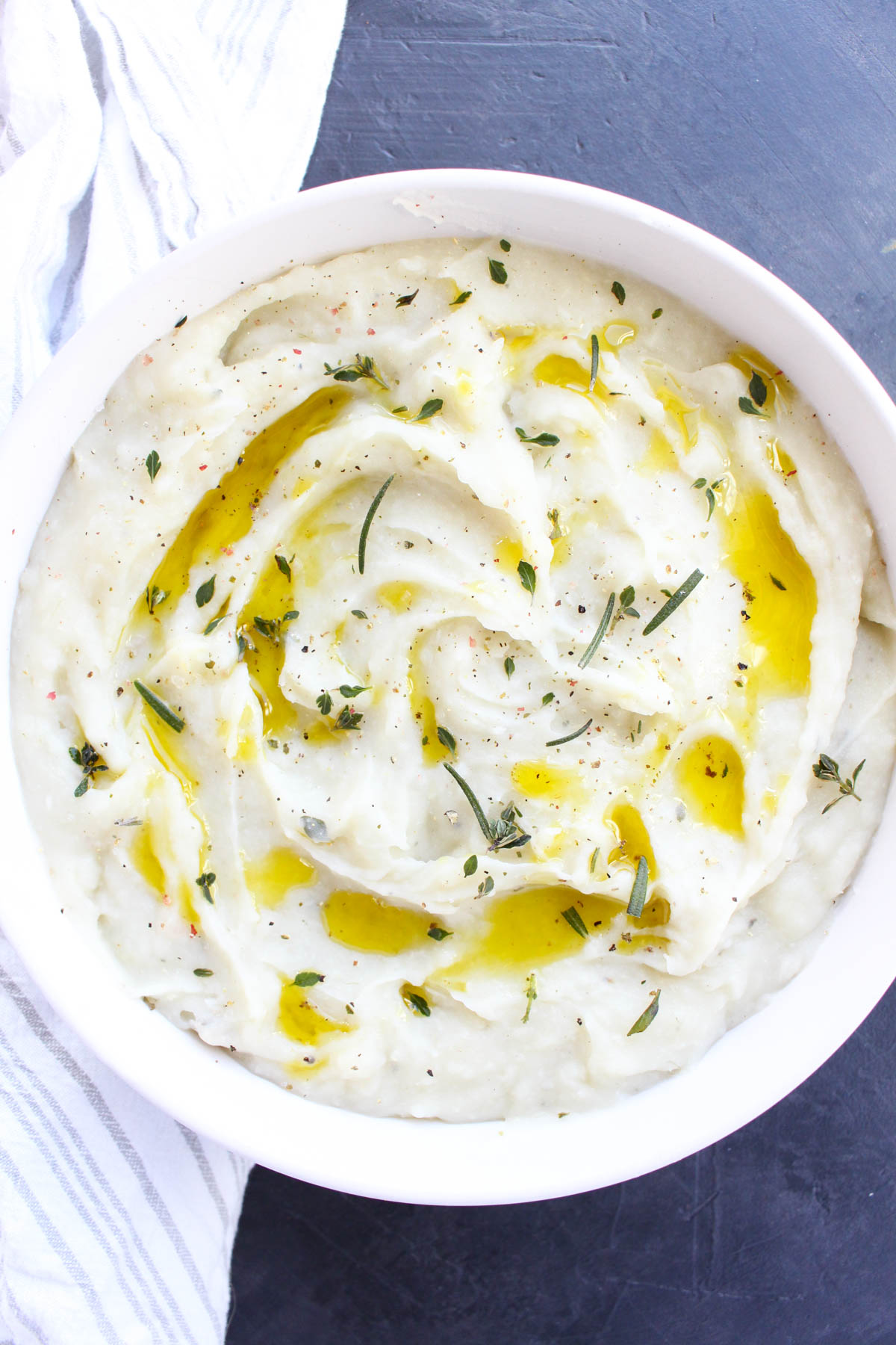 Overhead shot of serving bowl with creamy mashed potatoes topped with olive oil and fresh herbs.