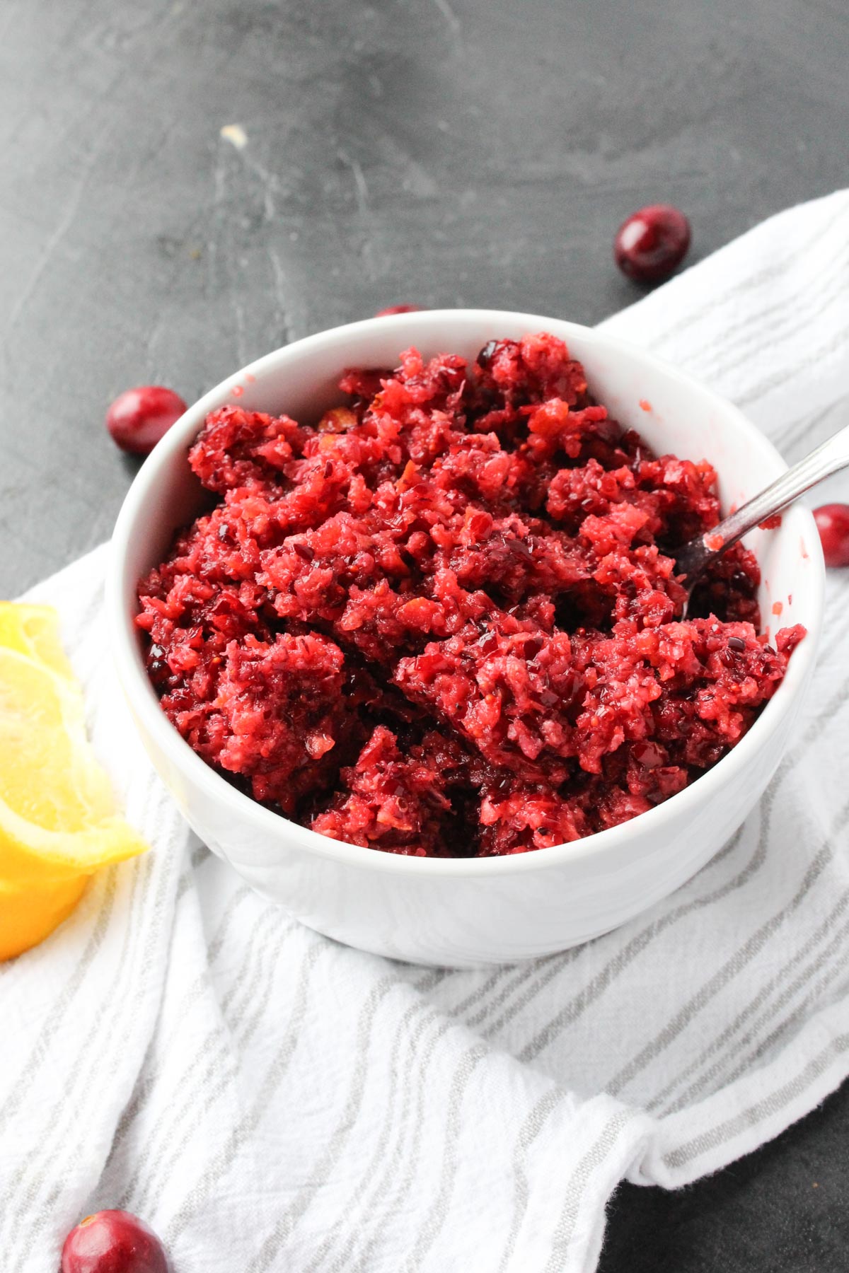 Easy Cranberry Relish in a white bowl on top of a striped dish towel with cranberries around the edges.
