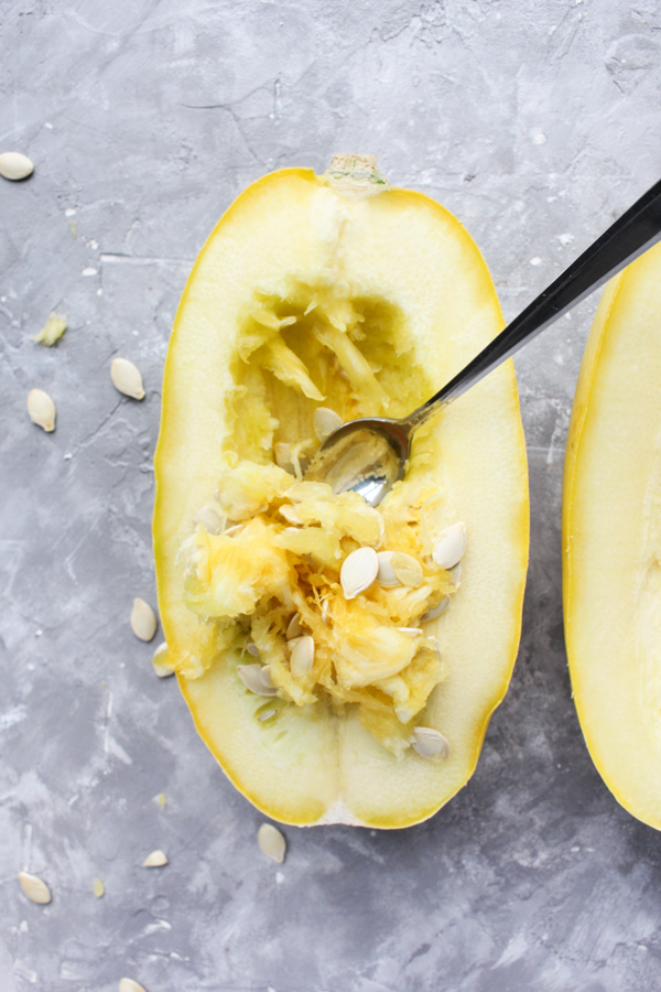 Spaghetti squash with spoon inside showing that you need to remove seeds.