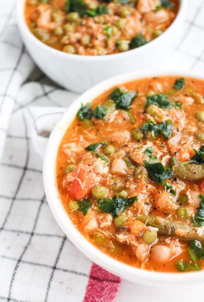 Two bowls of instant pot minestrone soup with fresh ingredients, broth, and herbs on top.