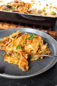 gluten-free lasagna with roasted tomato sauce on a plate with the baking dish in the background.