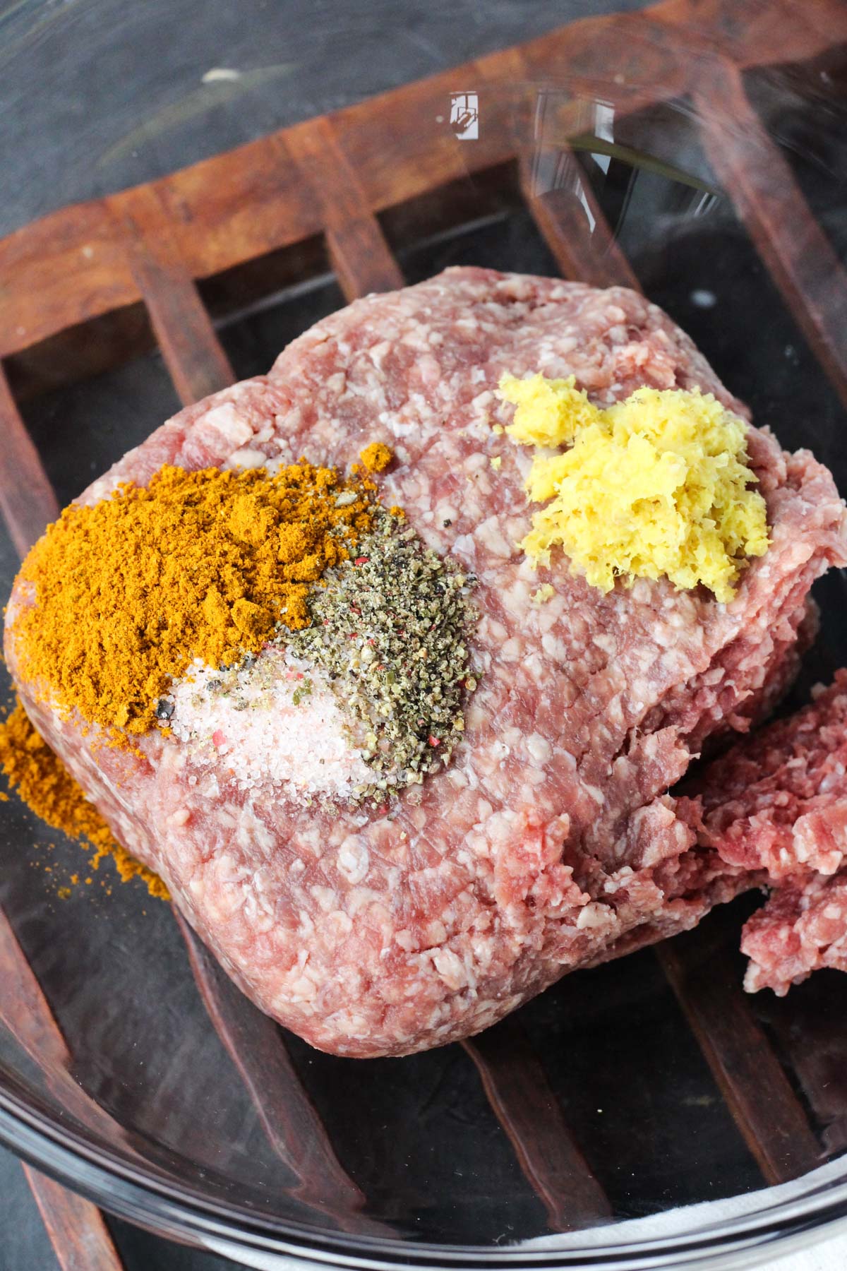 Ground beef in a glass bowl with spices on top.