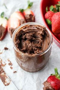 A mason jar with nut free chocolate spread surrounded by fresh strawberries.