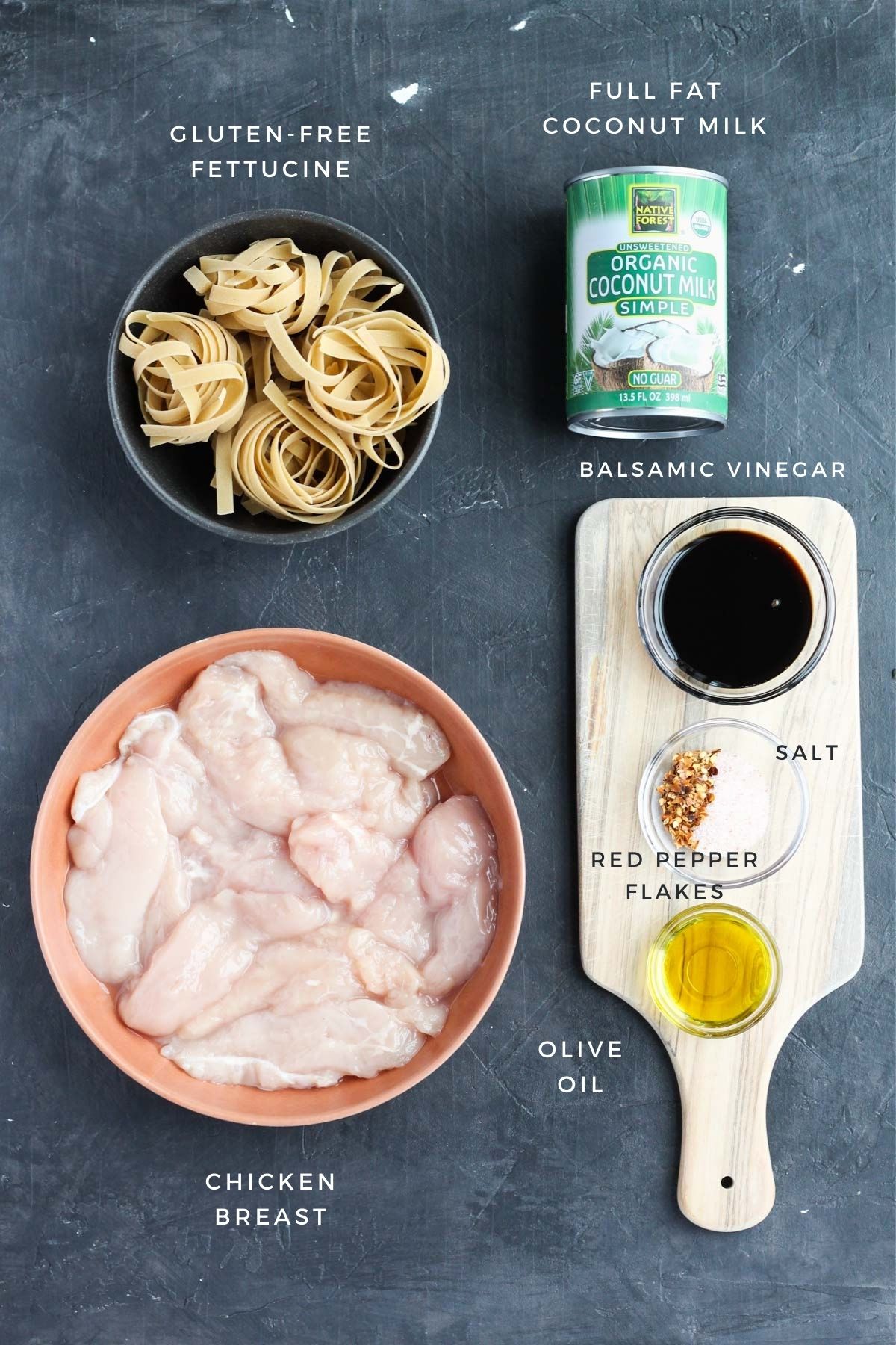 Wet ingredients, chicken breast, and gluten free pasta measured and laid out on a black counter.
