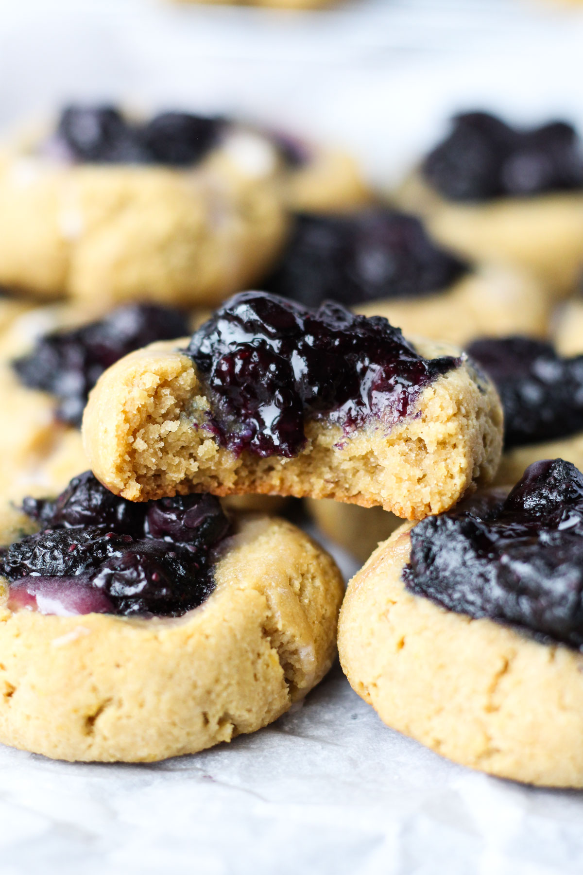 Big bite taken out of lemon blueberry thumbprint cookie stacked on top of other cookies.