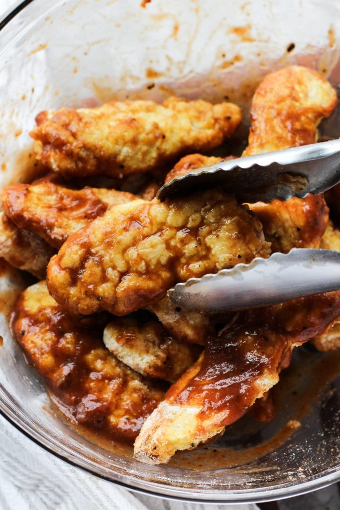Chicken tenders being tossed in bbq sauce.