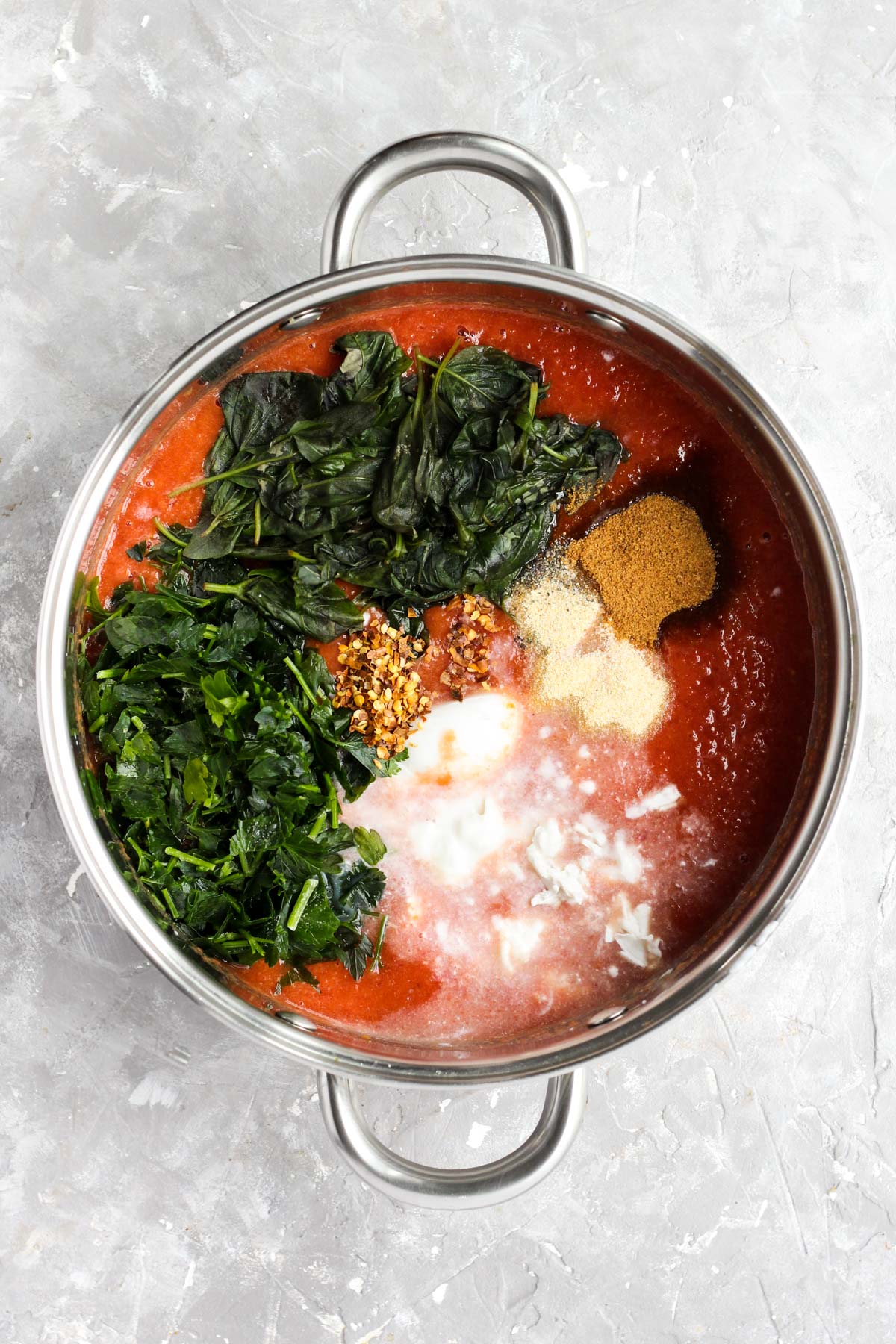 Sauce pan with pureed tomatoes and all herbs and spices on top.