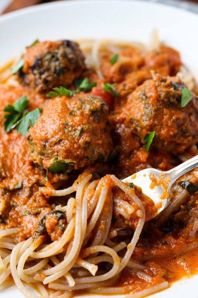 Close up picture of spaghetti and meatballs with sauce overtop.