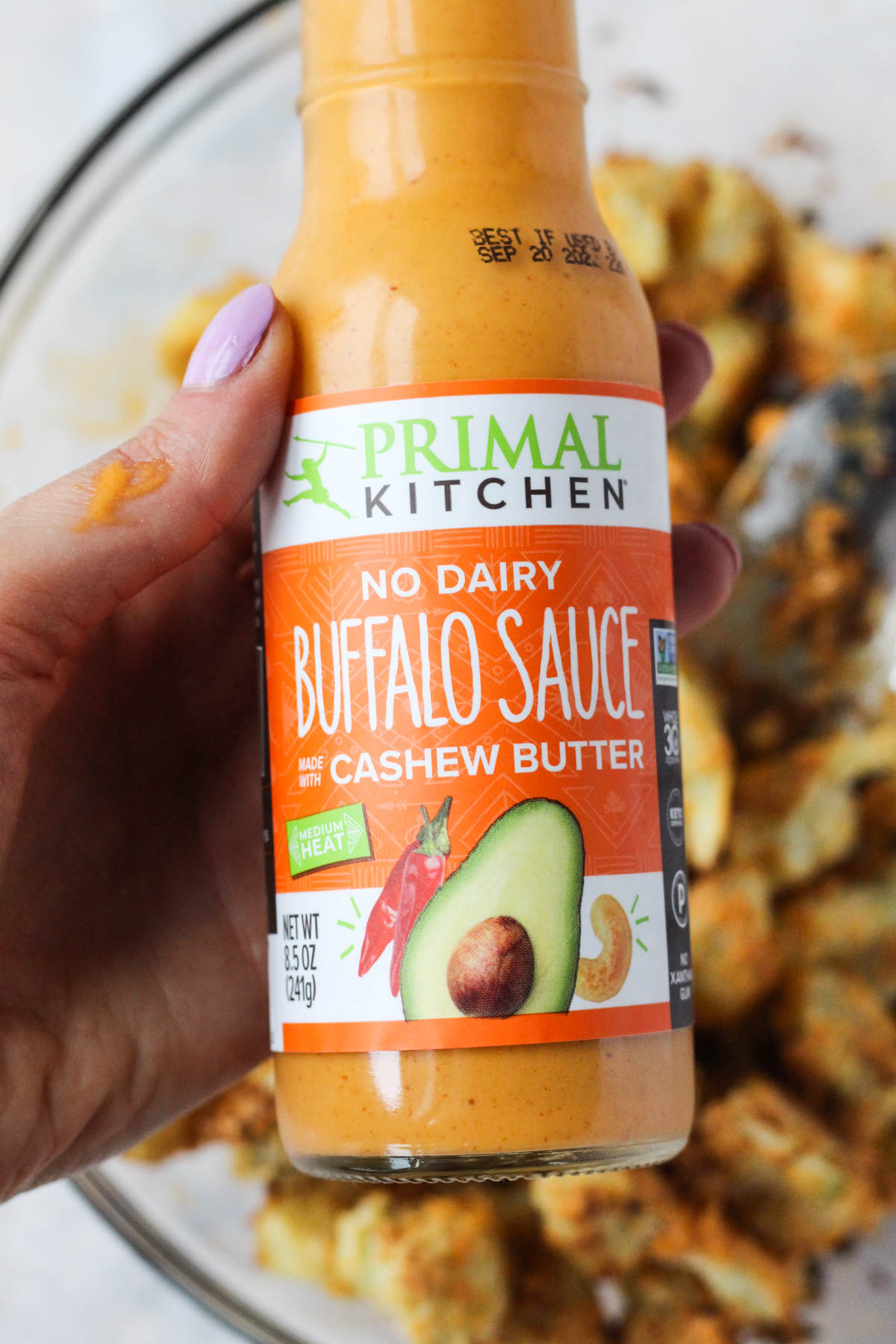 Hand holding primal kitchen buffalo sauce.