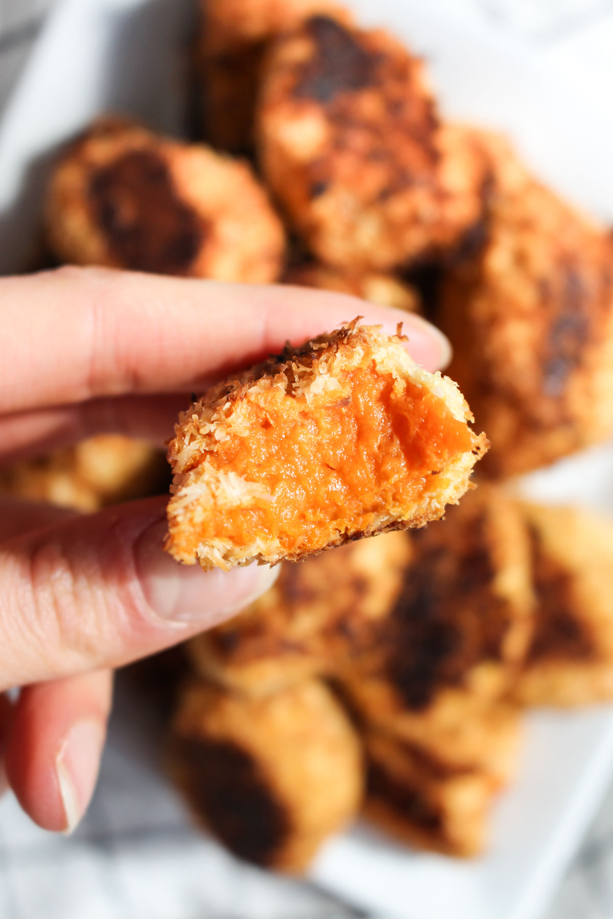 Hand holding sweet potato tot with a bite taken out.