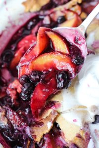 Spoon scooping out blueberry peach cobbler.