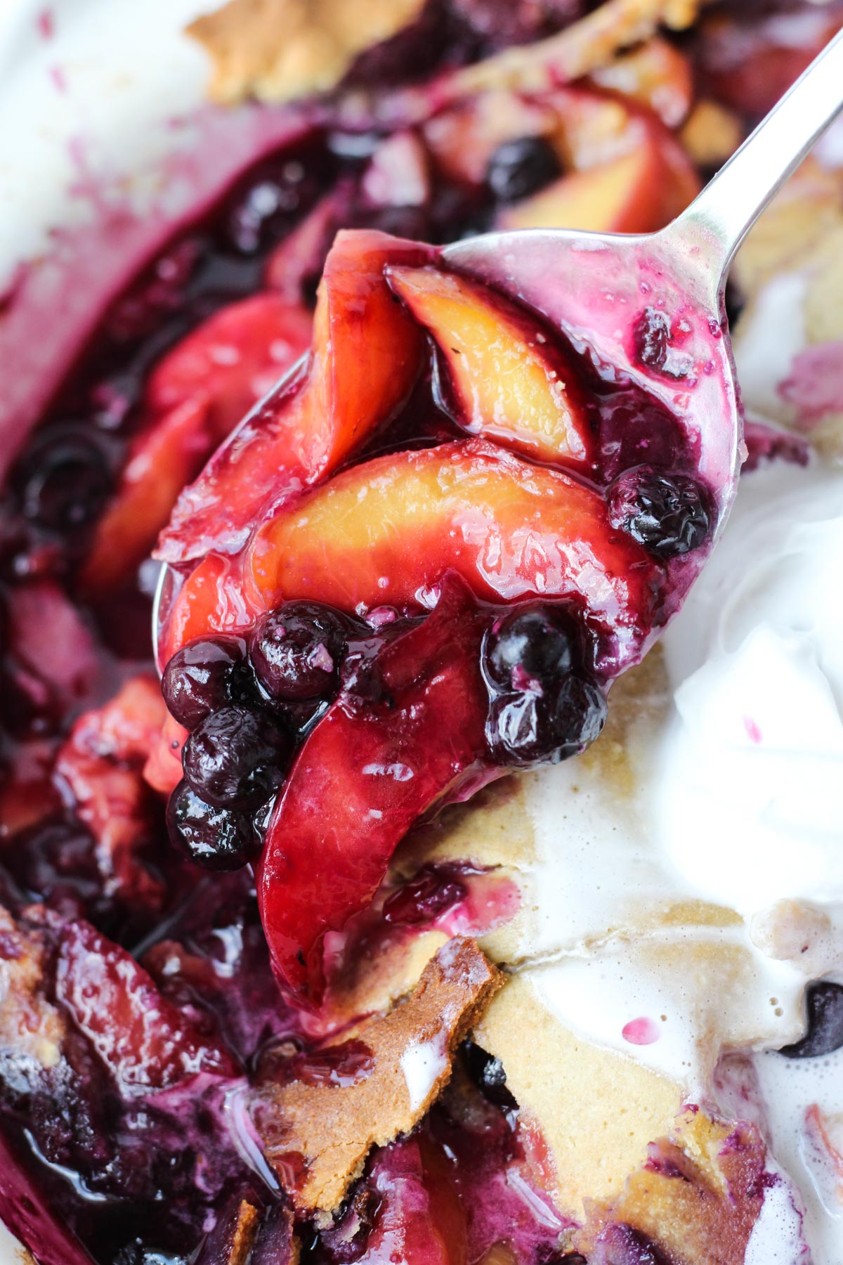 Spoon scooping out blueberry peach cobbler.