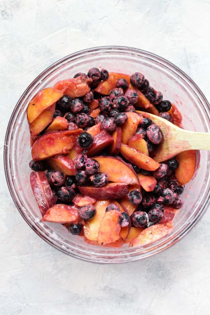 Fruit mixture in a mixing bowl with a wooden spoon.