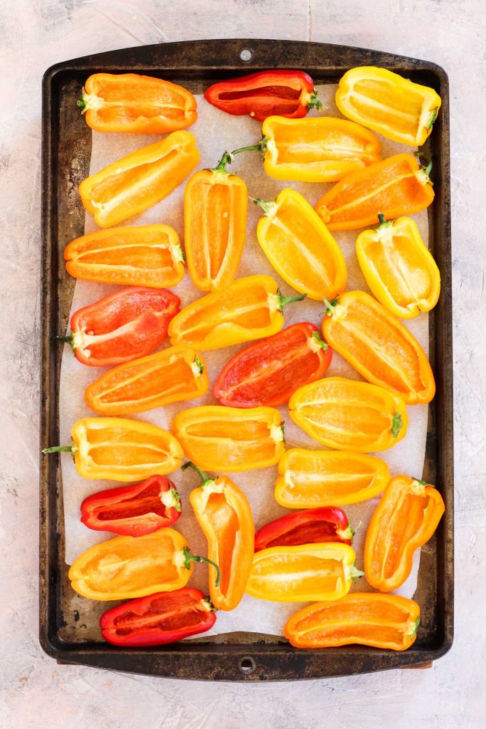 Baby peppers sliced in half on baking sheet.