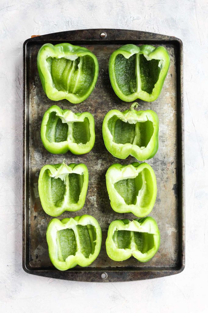 Bell peppers sliced in half and prepped on a baking sheet.