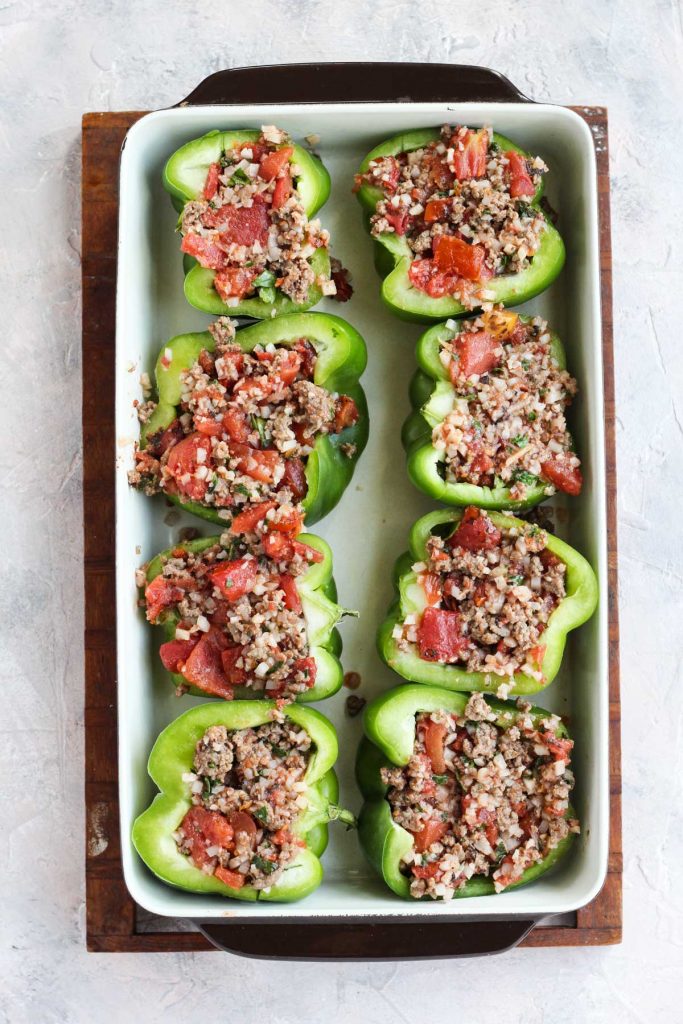 Bell peppers stuffed and ready to be baked in a casserole dish.