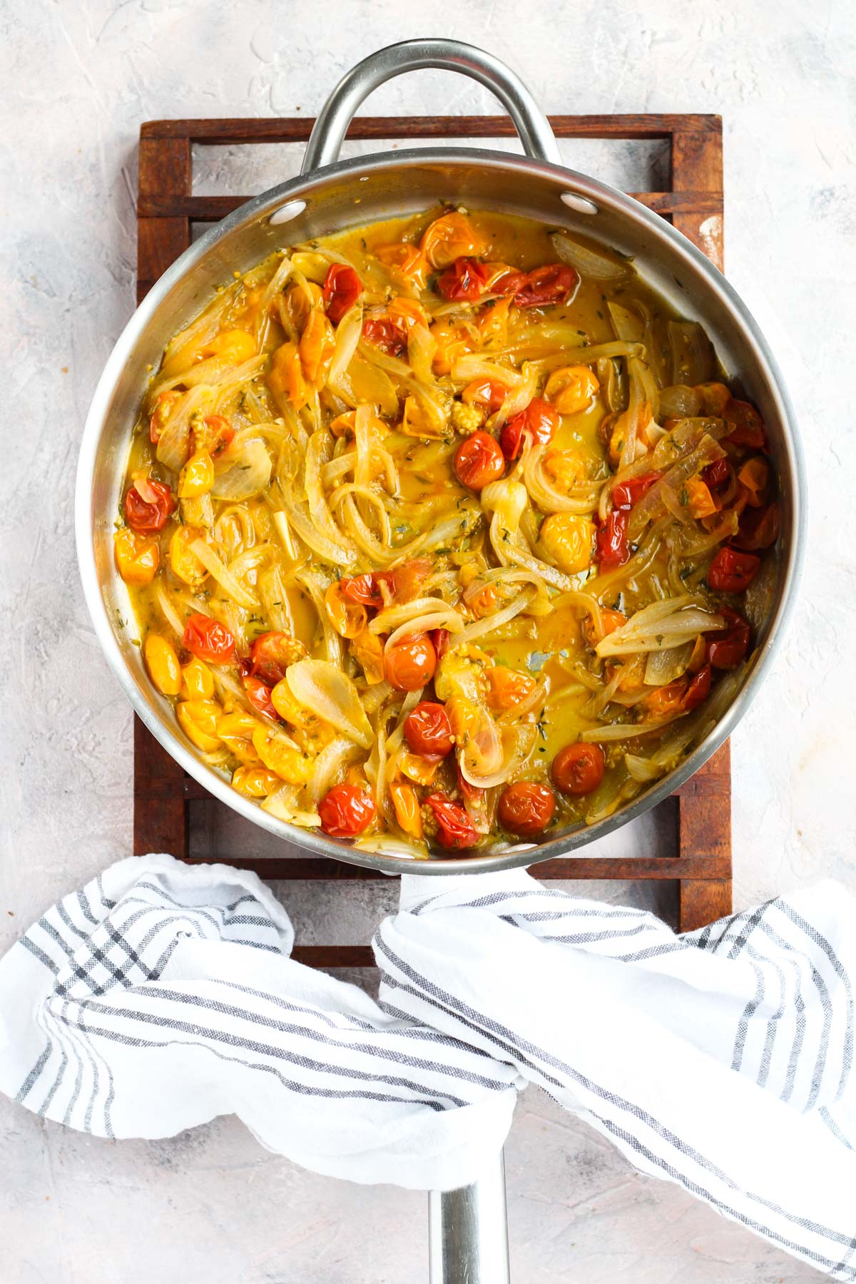 Caramelized onions with cherry tomatoes and herbs cooking in a pan. 