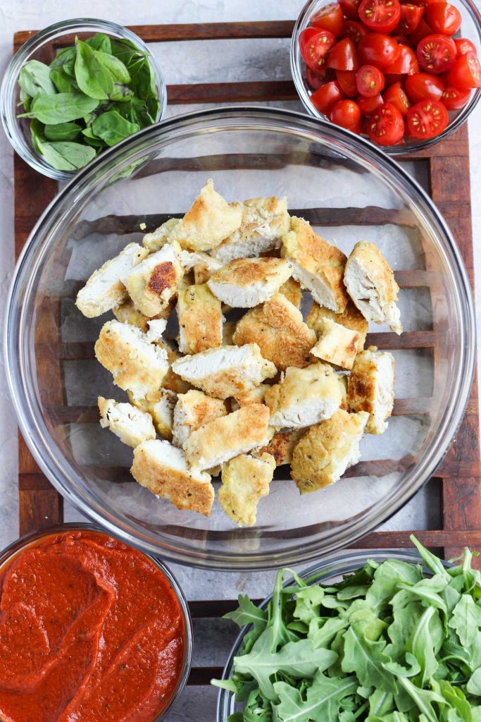 Chicken cutlets cut into small pieces in a glass bowl.