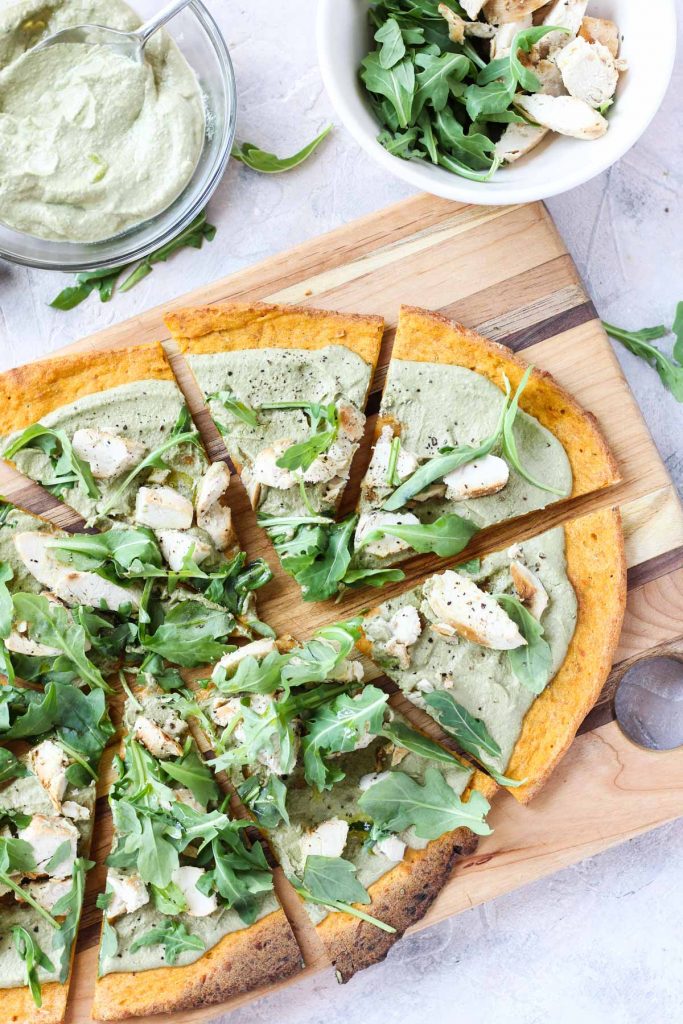 Overhead shot of pizza on wooden block with ingredients on the side.