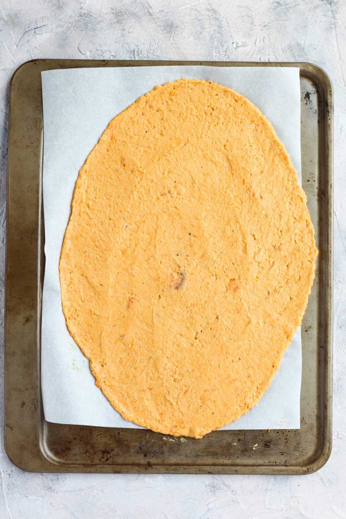 Pizza dough on parchment paper lined baking sheet.