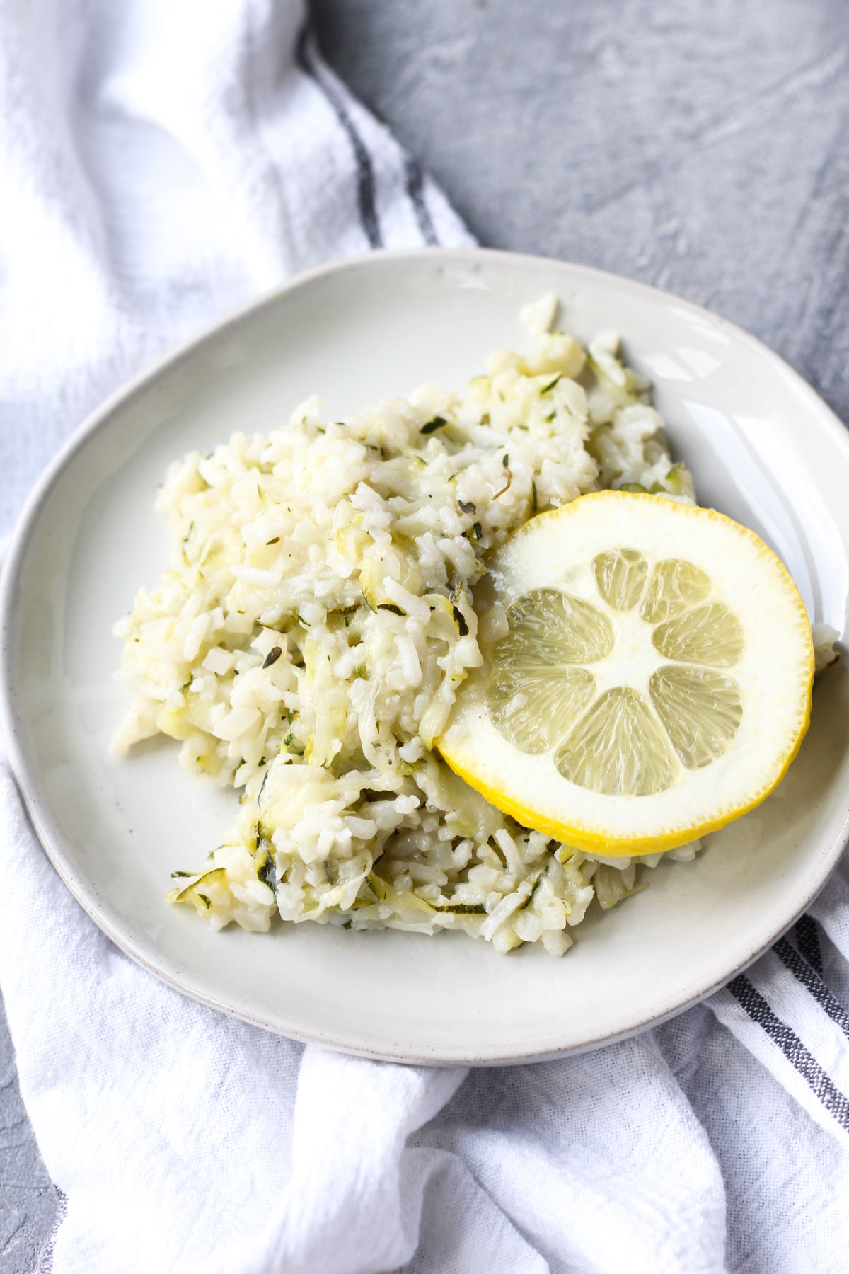 Plate with zucchini lemon risotto with a slice of lemon on the side.