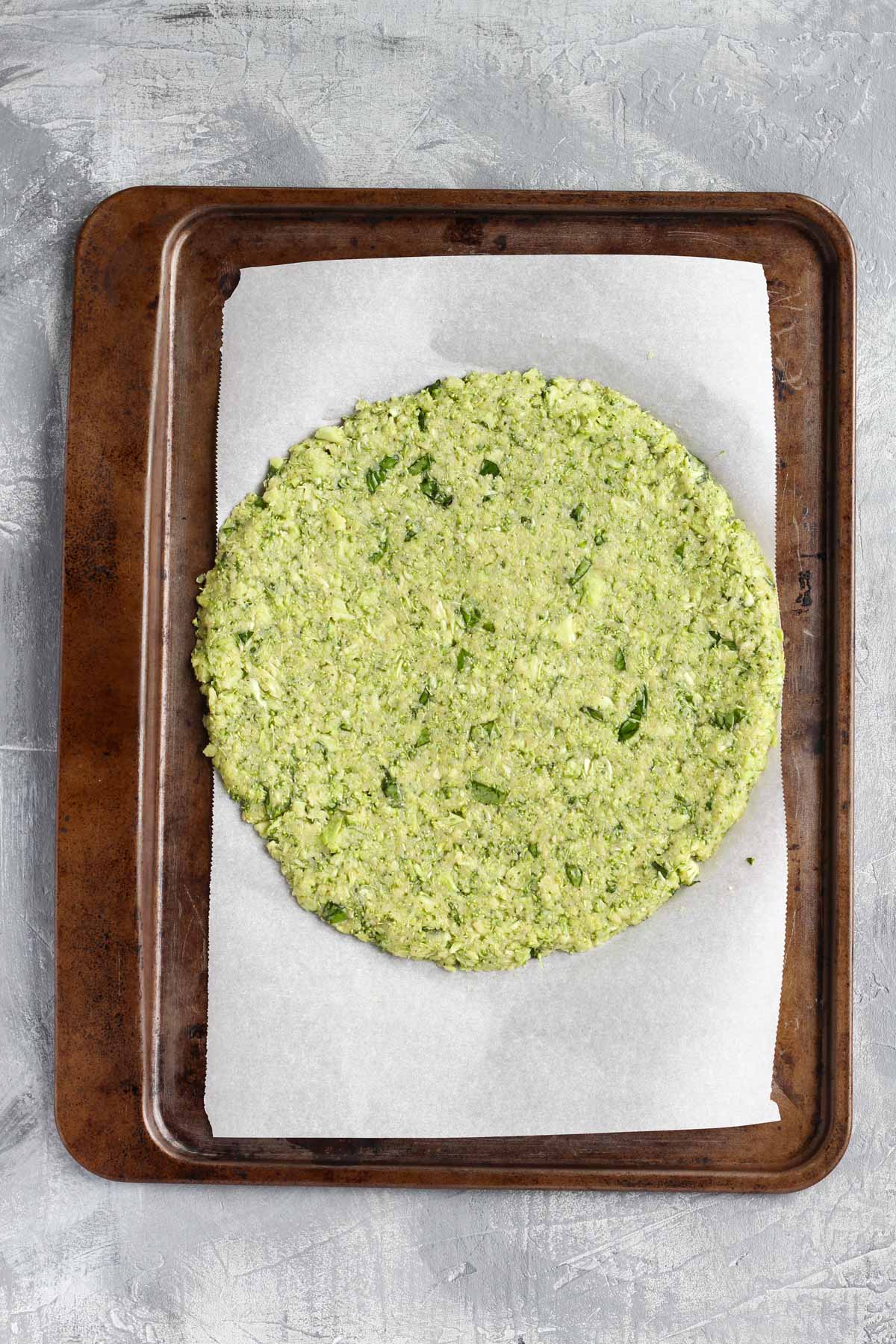 Round pizza crust pressed out on parchment paper on baking sheet.