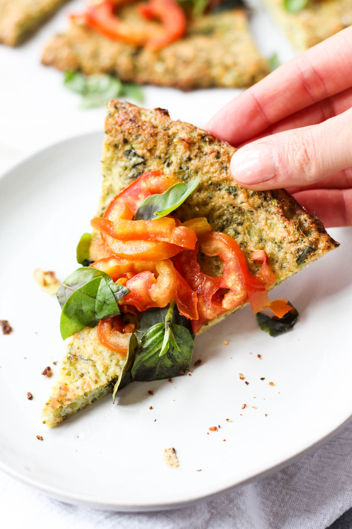 Hand holding slice of broccoli crust pizza.