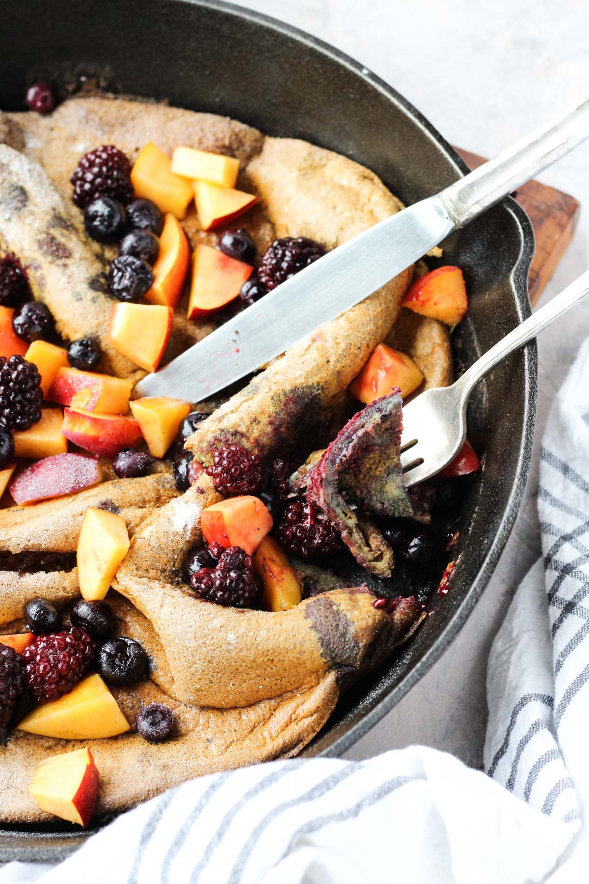 Side angle of fork and knife cutting a slice of the dutch baby.