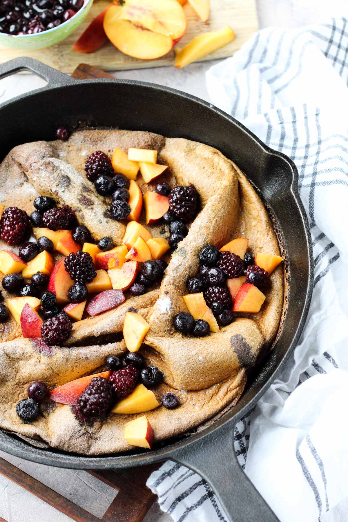 Side angle shot of dutch baby in cast iron skillet with fruit on top.