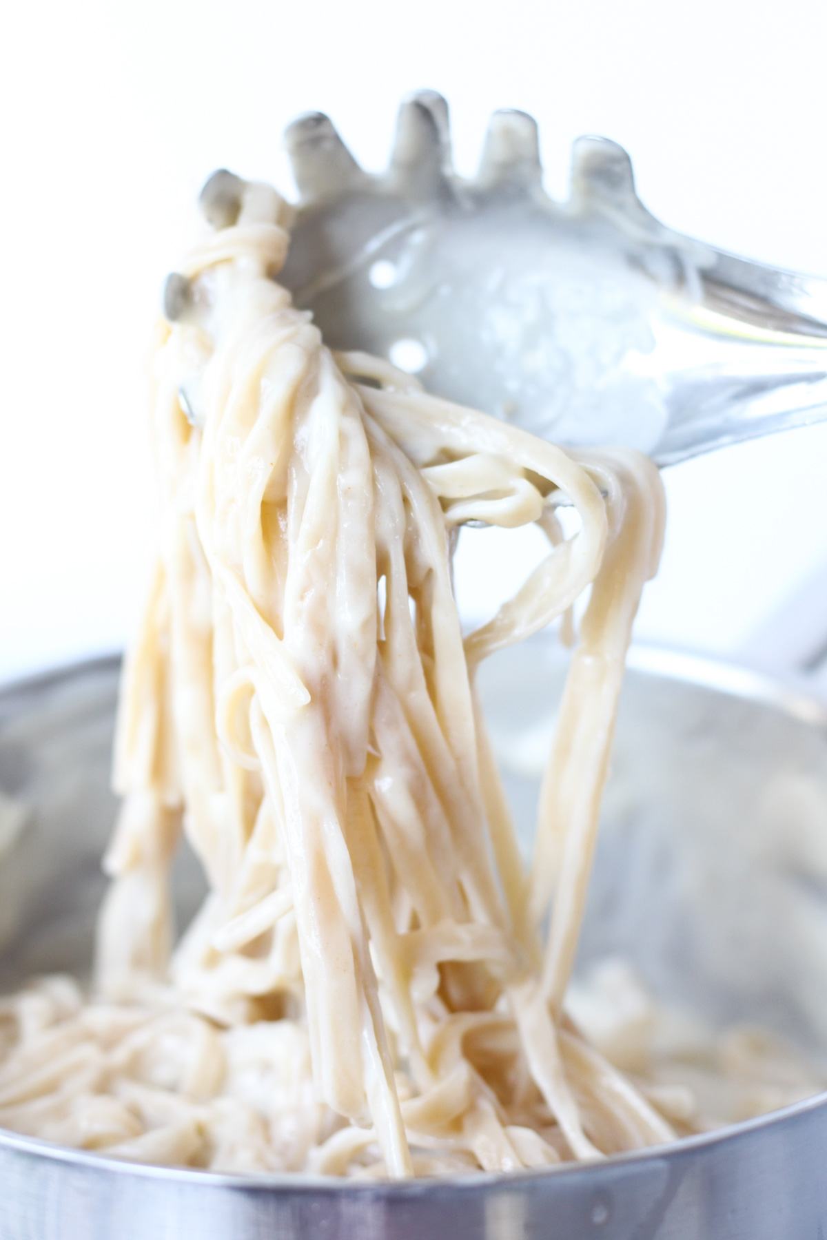 Serving spoon scooping out alfredo pasta from pan.