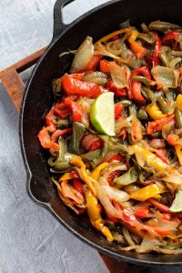 Close up picture of peppers and onions in cast iron skillet.