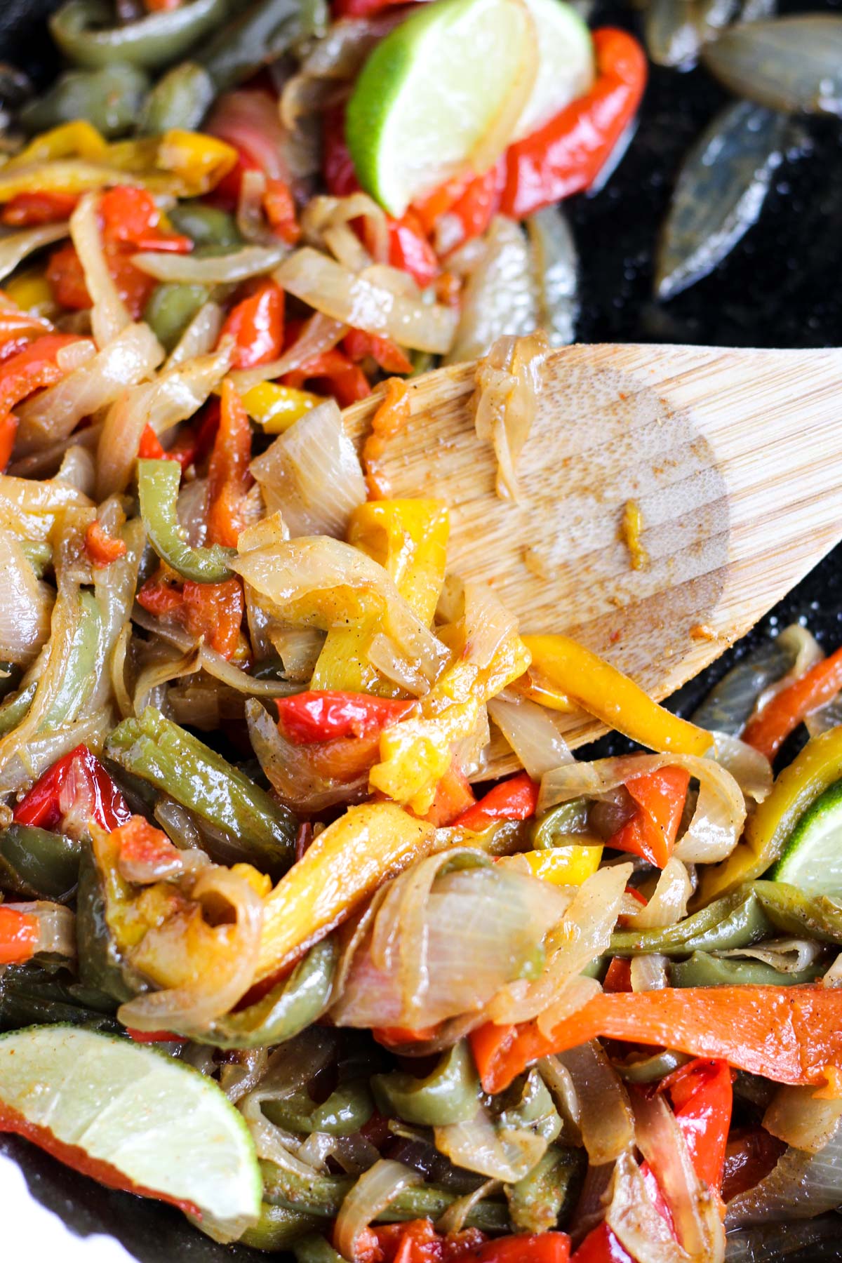 Wooden spoon scooping out peppers and onions.