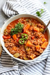 Bowl of beef chili topped with jalapeno slices.