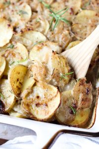 Casserole dish with wooden spoon scooping out scalloped potatoes.