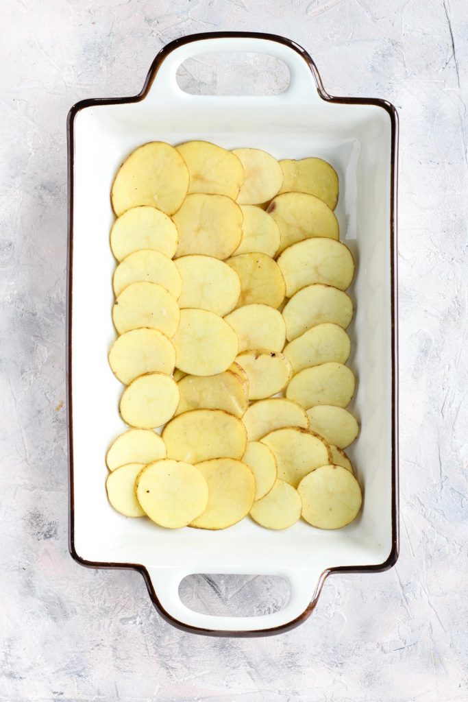 First layer of thinly sliced potatoes in casserole dish.