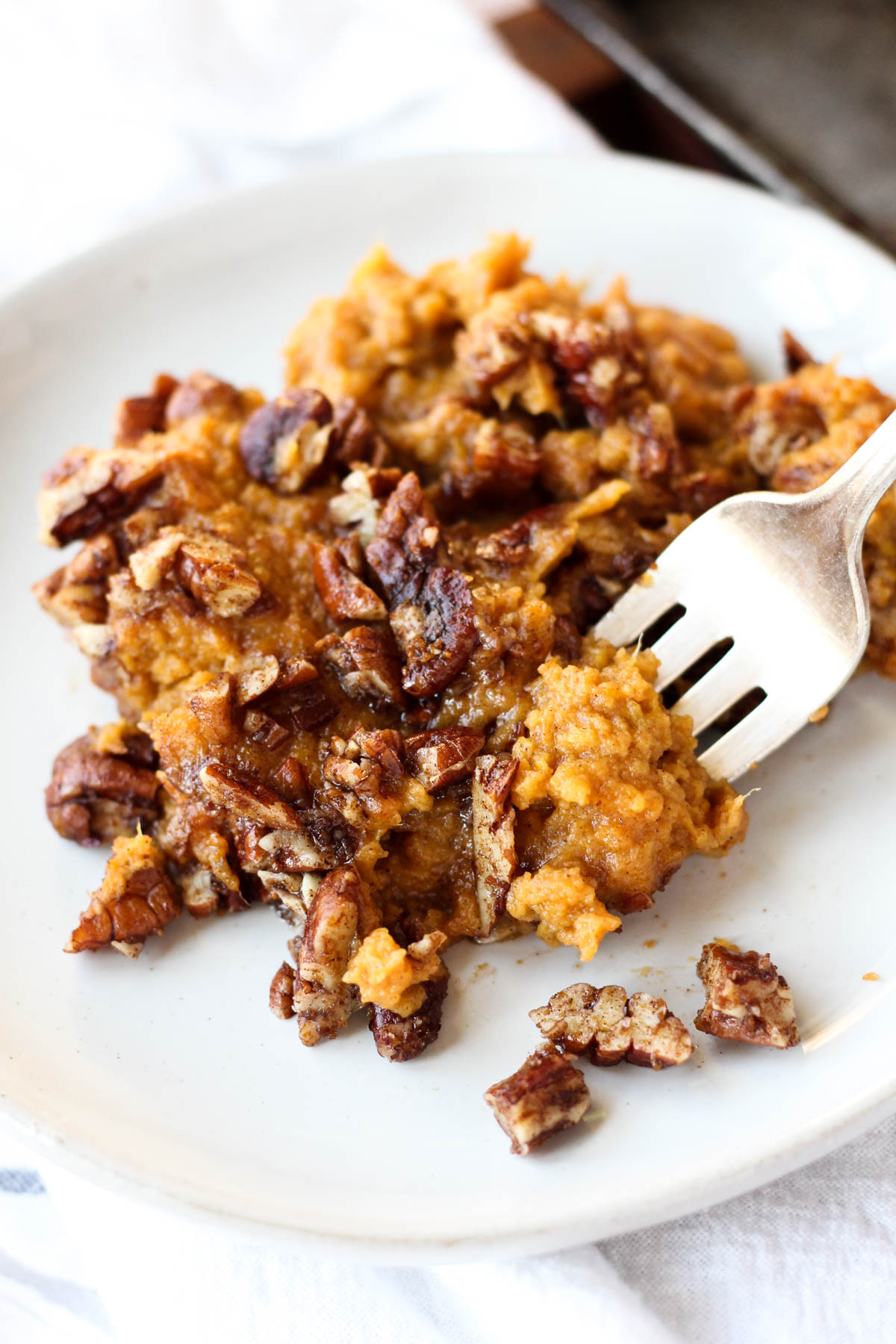 Fork scooping sweet potato casserole off a white plate.