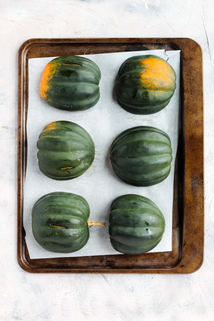 Acorn squash cut in half facing down on baking sheet.