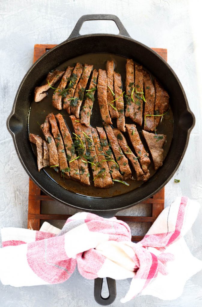 Sliced steak in cast iron skillet.