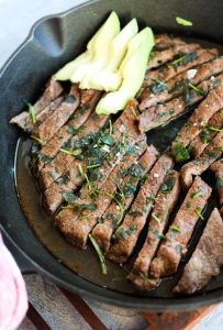 Close up picture of baked fajita steak in a cast iron skillet.