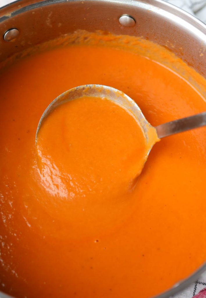 Ladle scooping out tomato carrot soup.