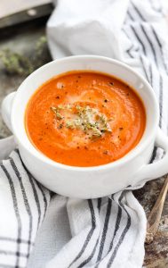 White bowl of tomato carrot soup with fresh thyme on top.