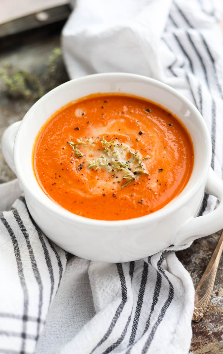 White bowl of tomato carrot soup with fresh thyme on top.