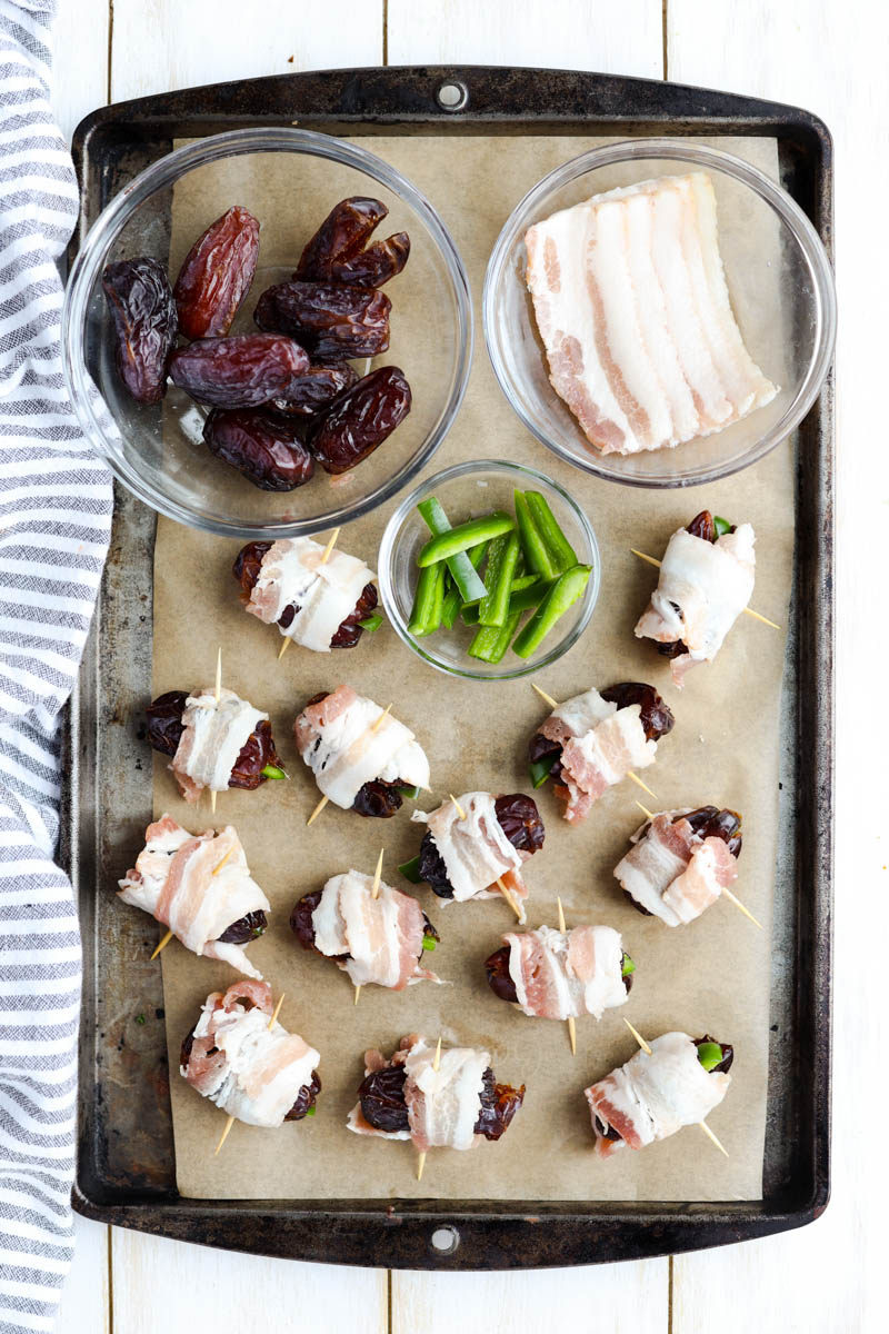 Bacon wrapped dates on a baking sheet with ingredients.