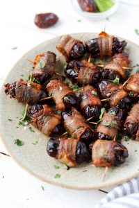 Dates with crispy bacon wrapped around them on a plate.