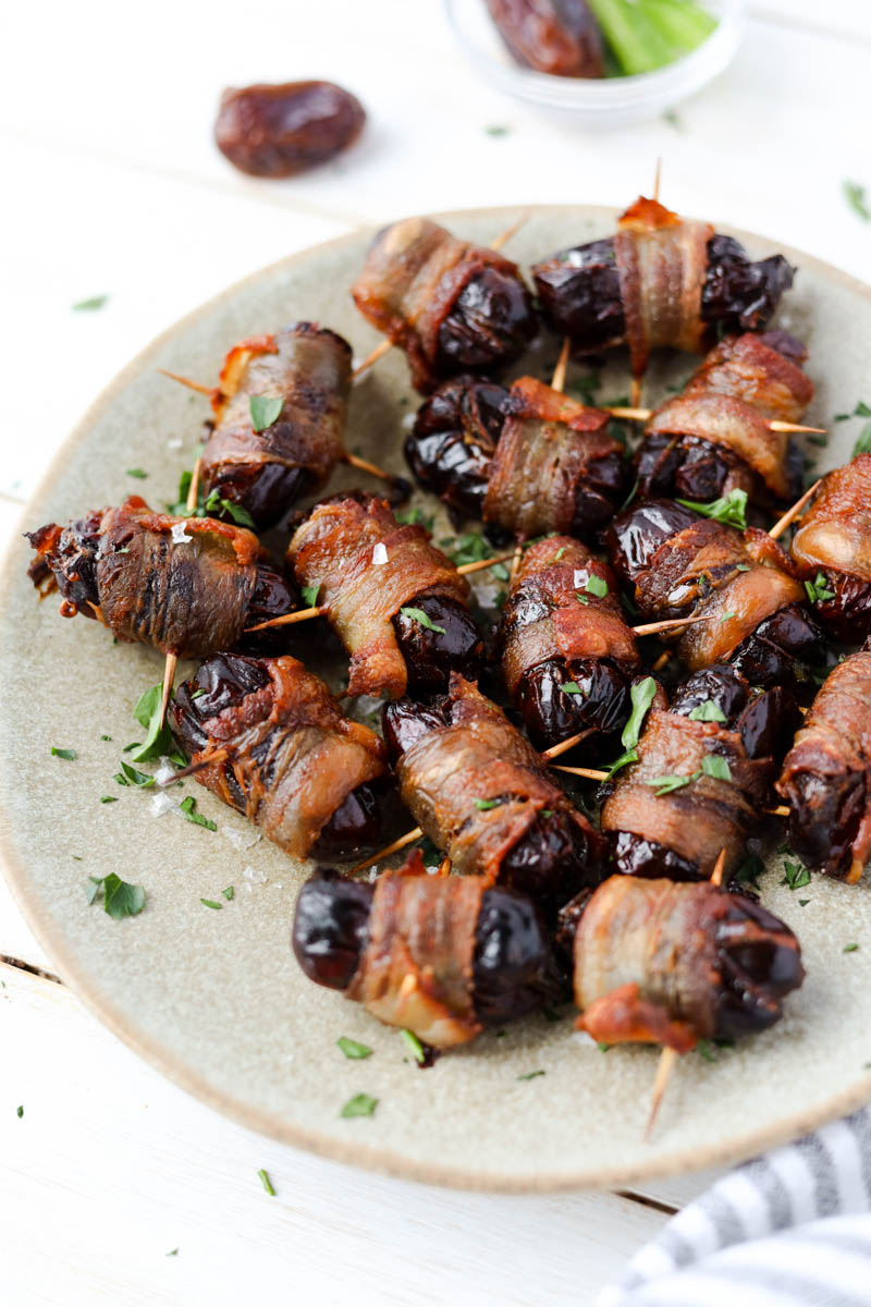 Dates with crispy bacon wrapped around them on a plate.