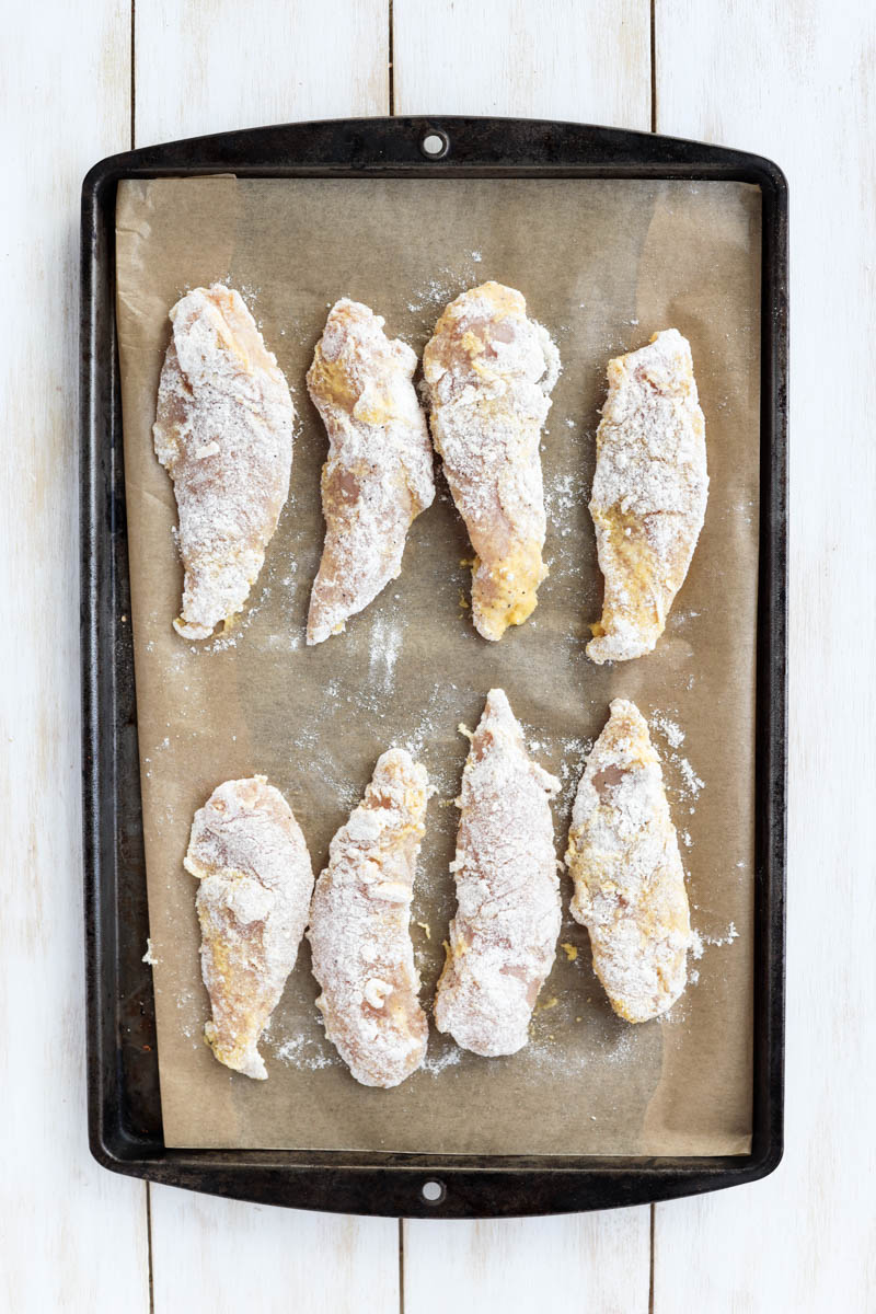 Breaded chicken tenders on a parchmetn paper liend baking sheet.