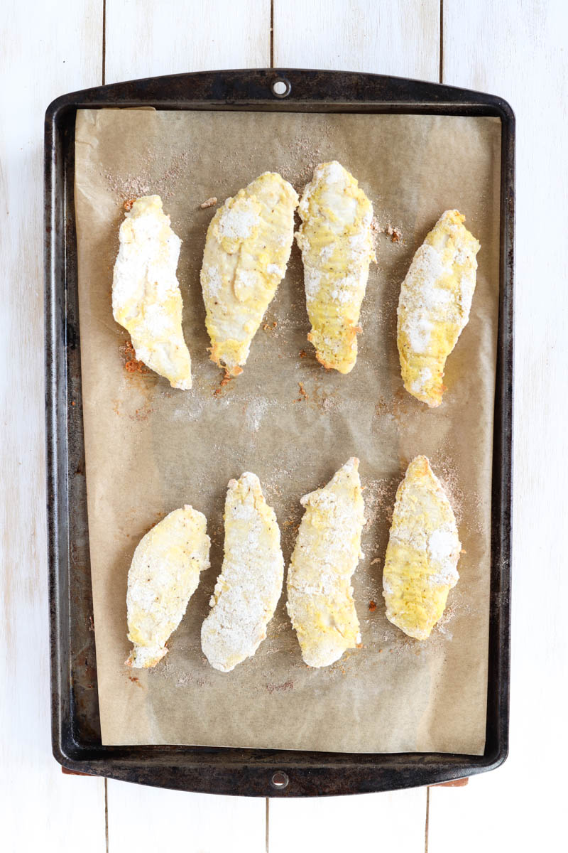 Baked chicken tenders on a parchment paper lined baking sheet.