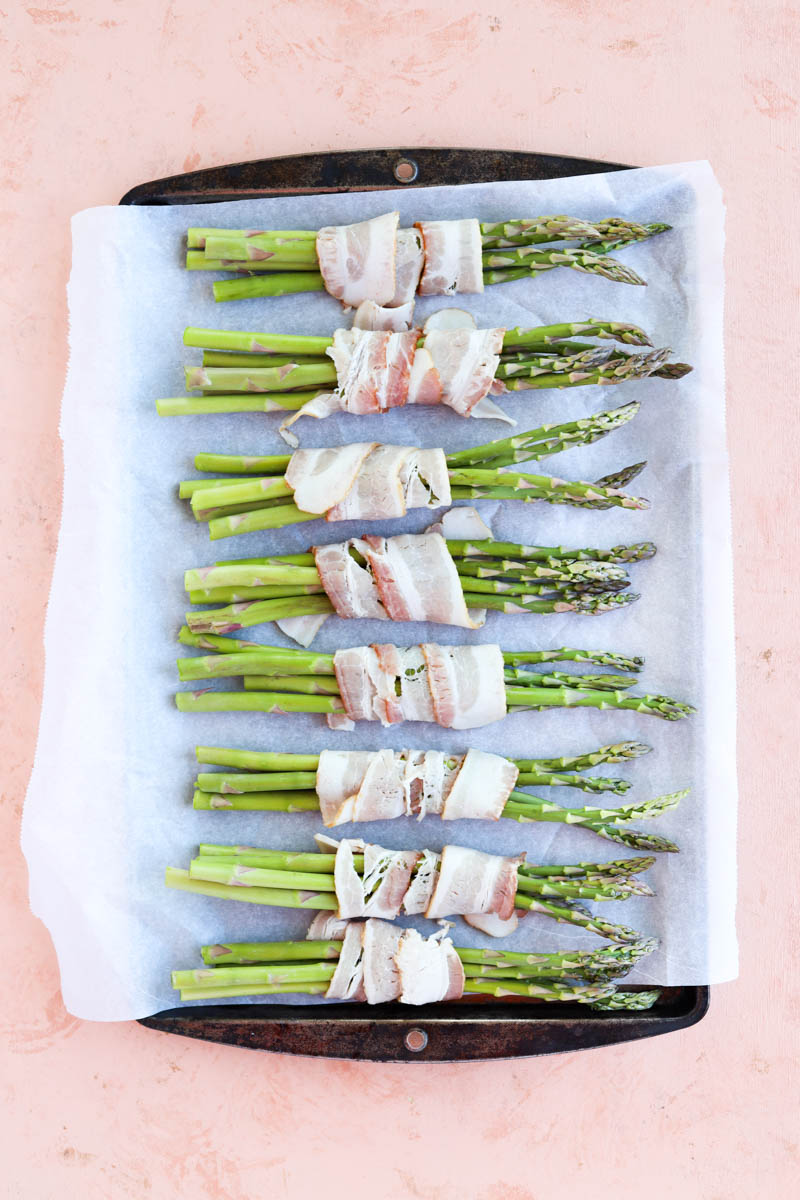 Bacon wrapped asparagus on a parchment paper lined baking sheet.