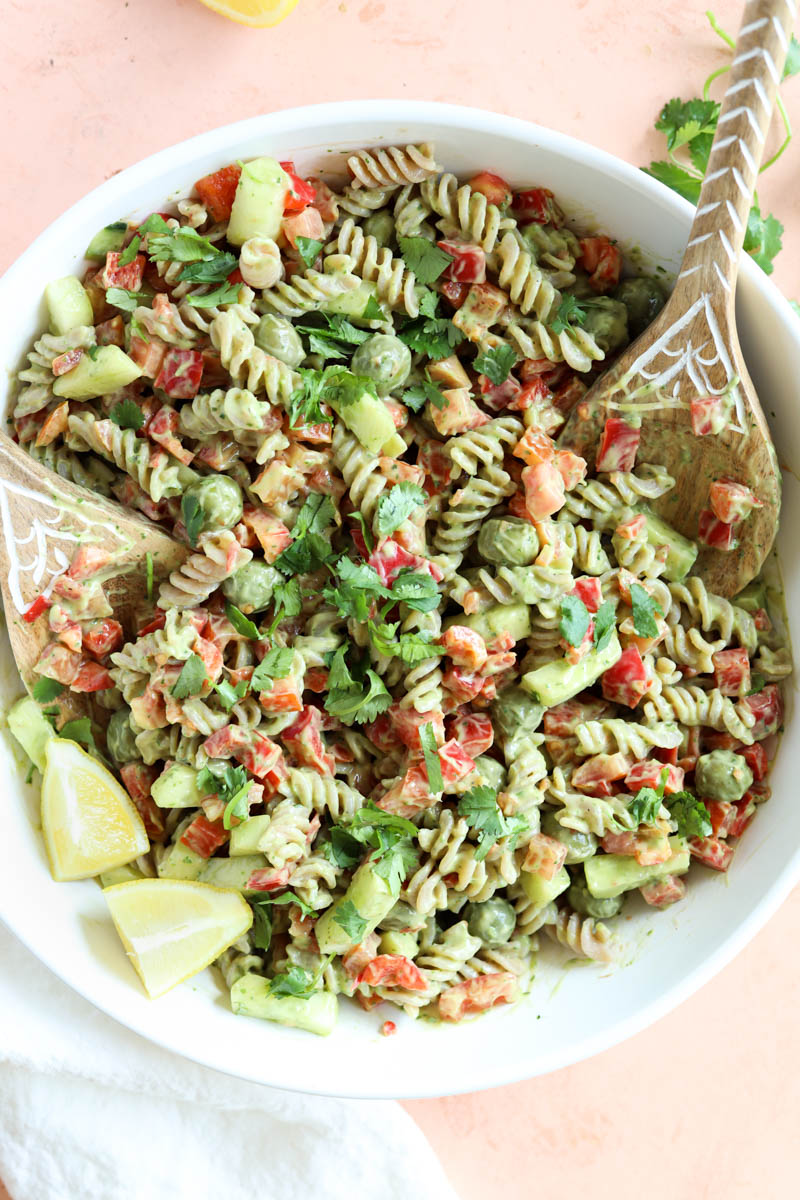 Finished pasta salad in white bowl with wooden serving spoons.