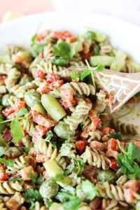 Wooden spoon scooping out creamy avocado pasta salad.